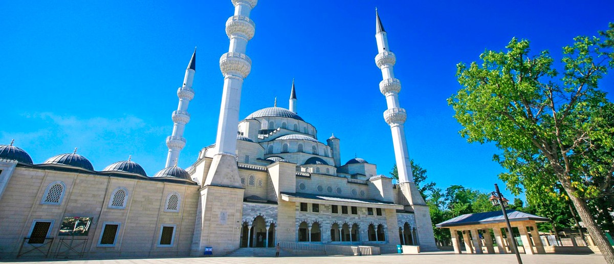 A grand mosque with multiple domes and tall minarets stands against a clear blue sky.