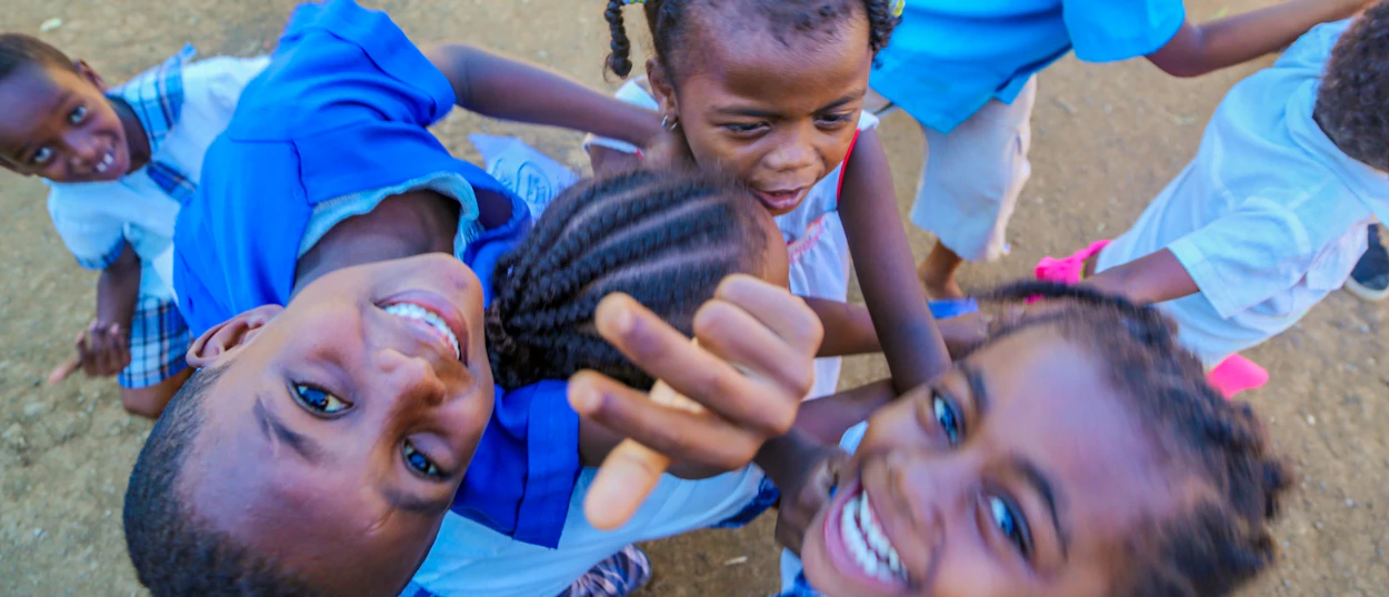 Joyful children with braided hair look up at the camera, smiling and reaching out playfully.