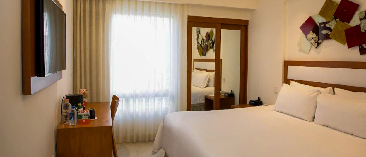 A bright and comfortable hotel room in Cancun with a large bed, desk, and window.
