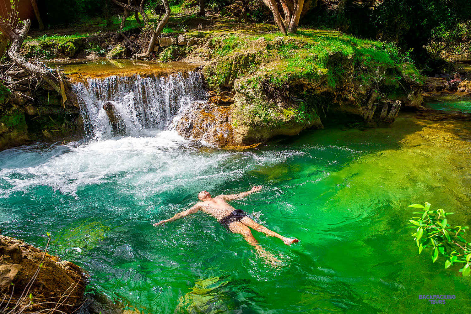 A swimmer floats in a clear green pool below a cascade at the Akchour Waterfalls.