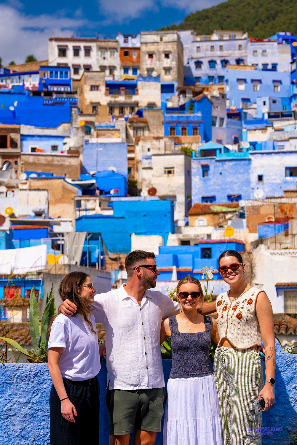 Four friends smile together on a terrace above the blue buildings of Chefchaouen.
