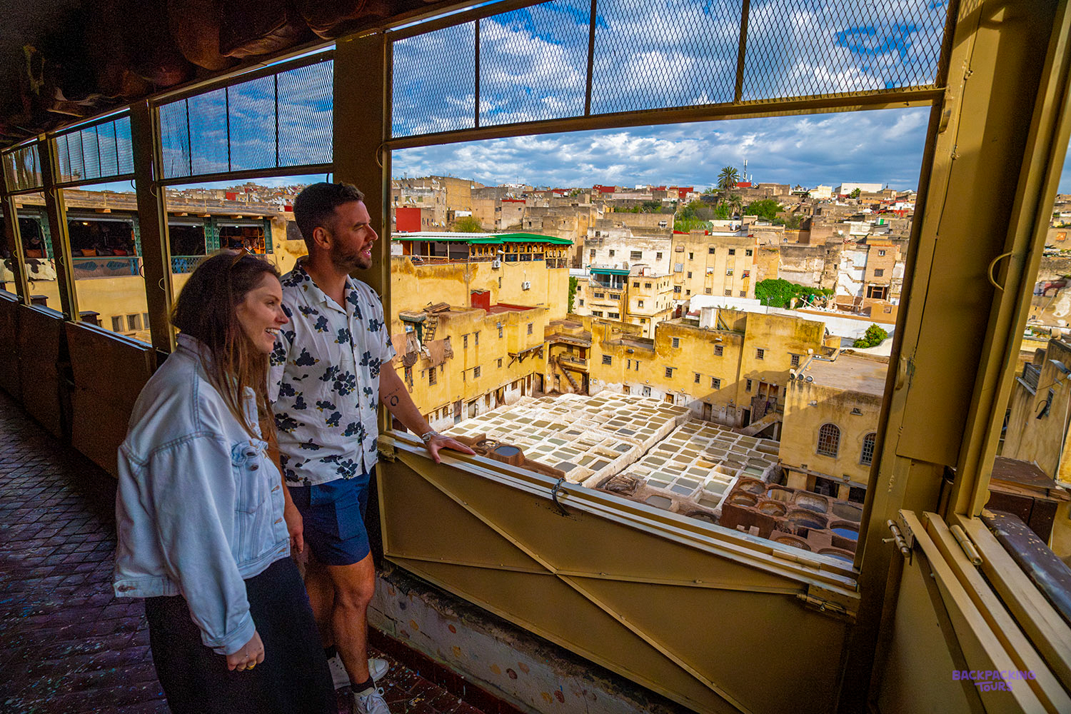 Two travellers look out from a window over the dyeing pits of a Fes tannery and the old city.
