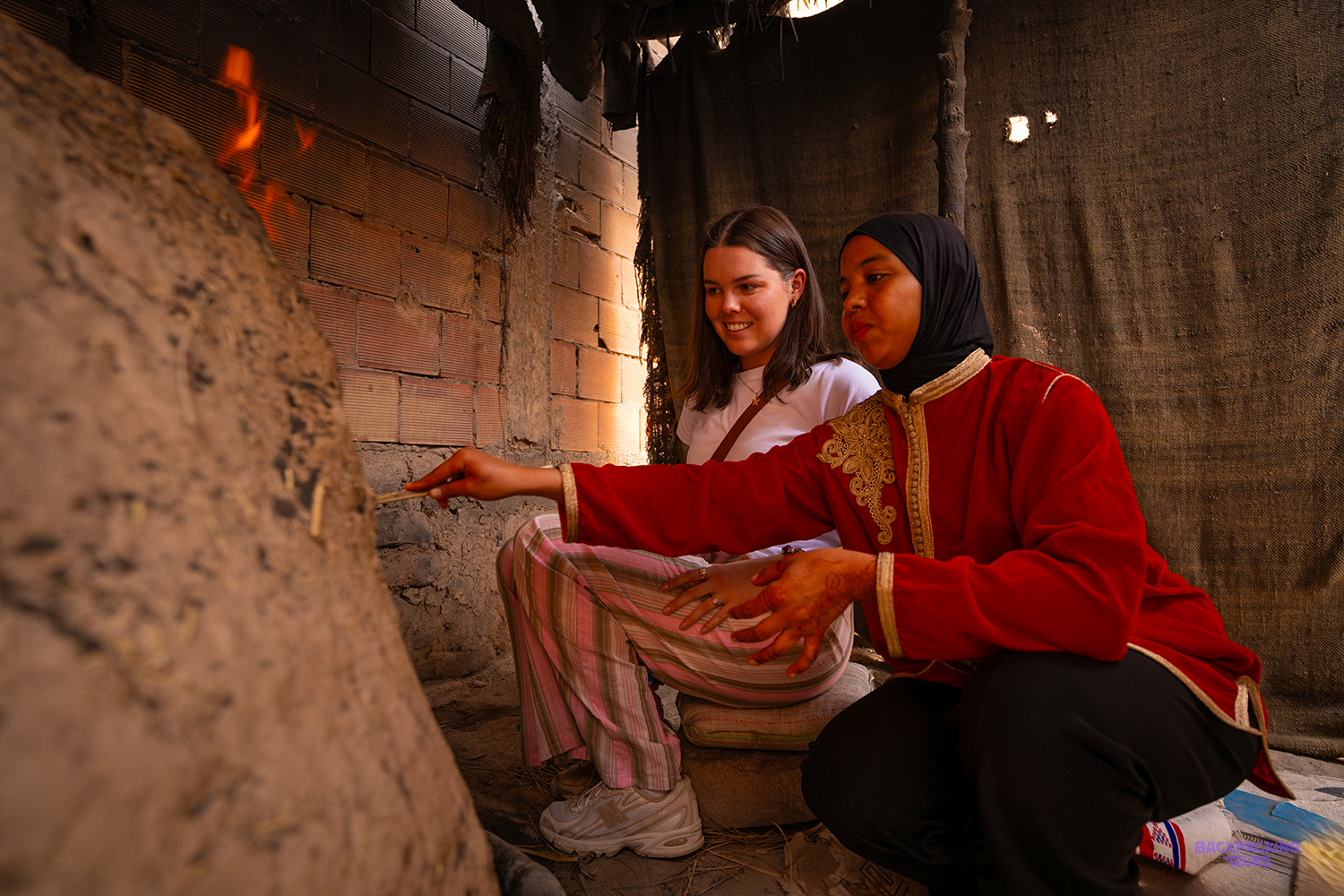 A local woman shows a traveller how bread is baked in a traditional clay oven.