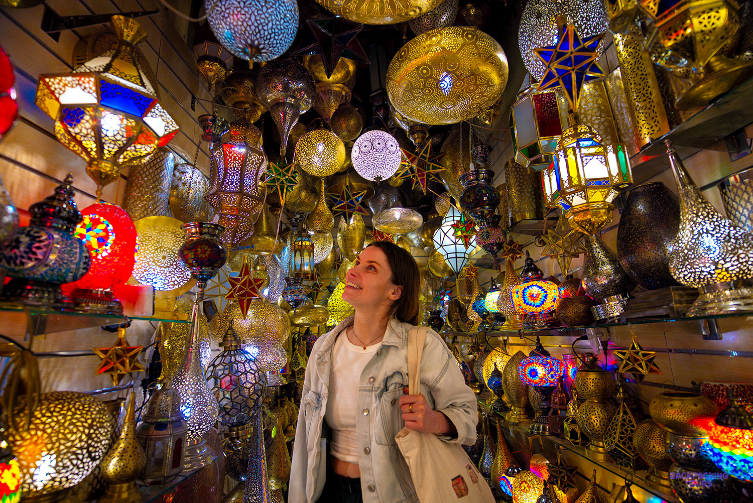 A traveller looks up at hundreds of glowing metal lanterns in a shop in the Marrakech medina.
