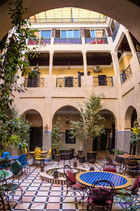 The courtyard of Riad Omar in Marrakech, with arched galleries, plants and tiled tables.