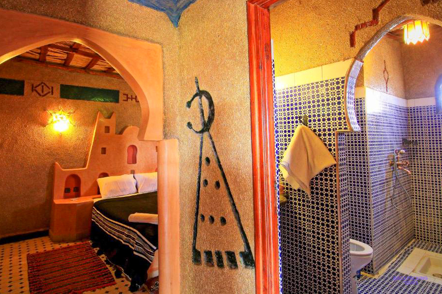 A room at Dar Tafouyte Riad in Merzouga with earthen walls and a tiled bathroom.