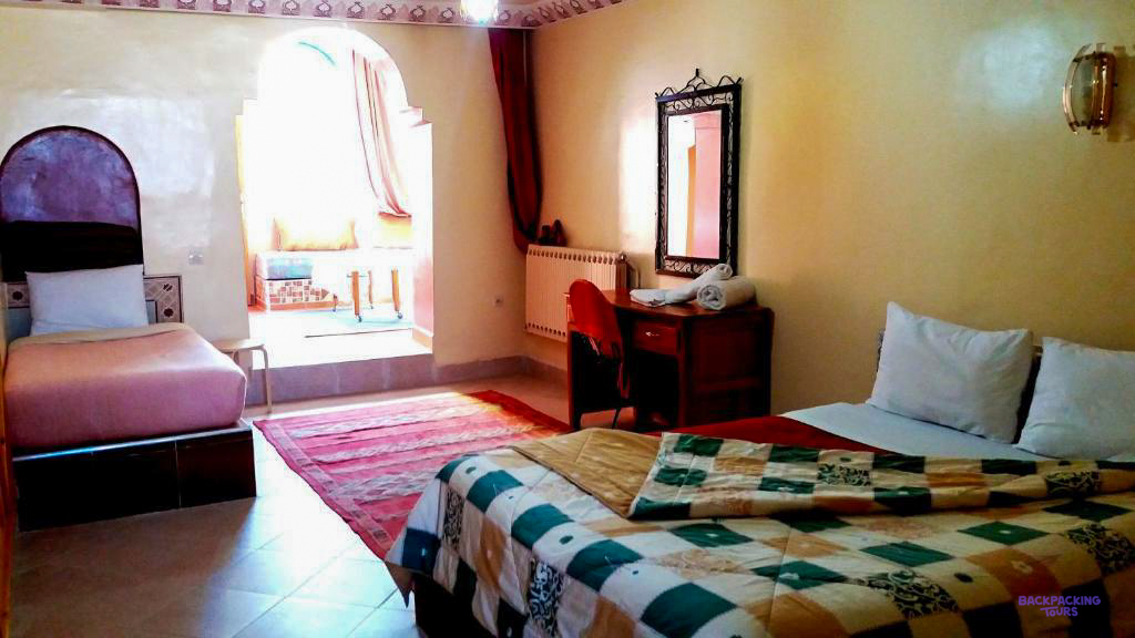 A guest room at Ksar Timnay Hotel in Midelt with a double bed, a single bed and a patterned rug.