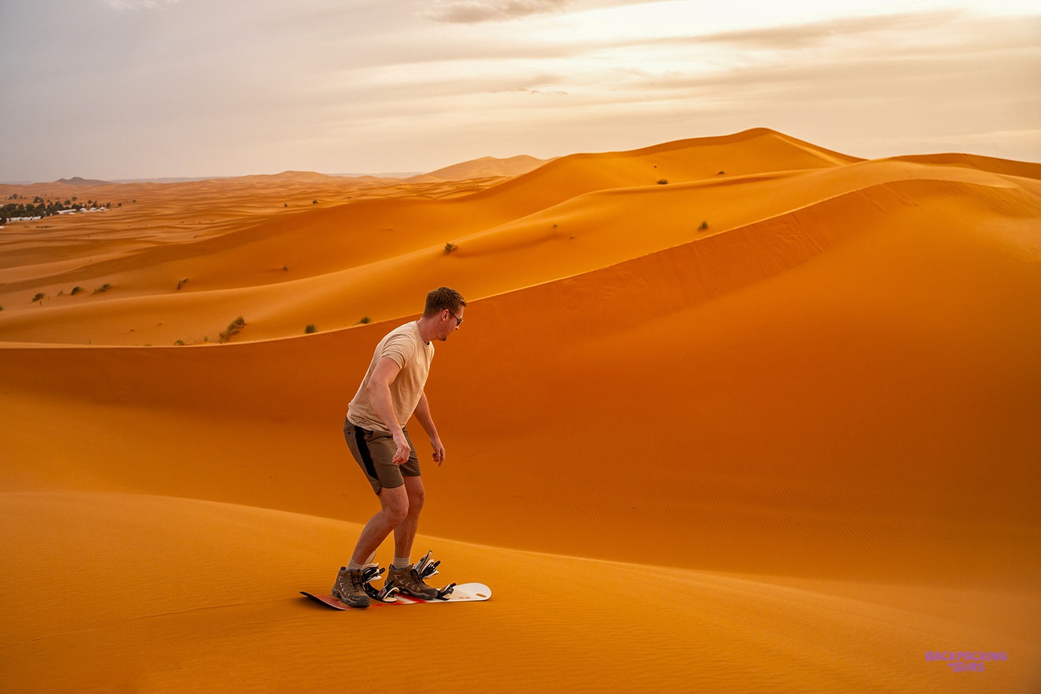 A traveller sandboards down a smooth orange dune in the Sahara.