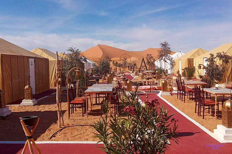 Rows of tents and dining tables at Tafouyte Camp, with a tall Sahara dune rising behind.