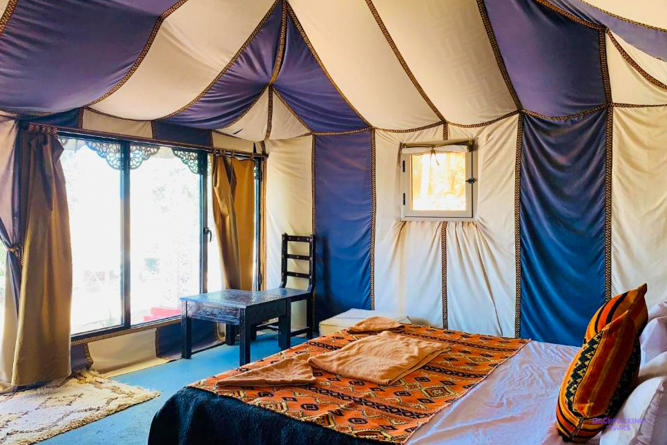 Inside a tent at Tafouyte Camp in the Sahara, with a made-up bed and a patterned blanket.