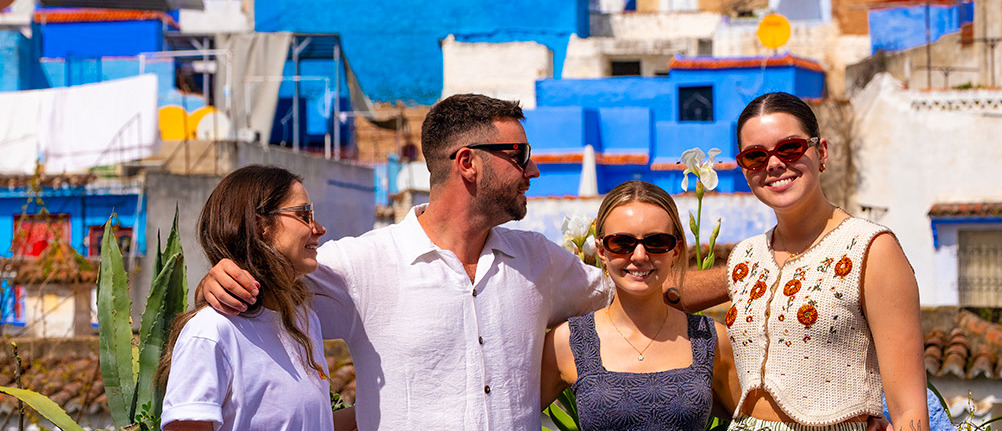 Four friends smile together on a terrace above the blue buildings of Chefchaouen.