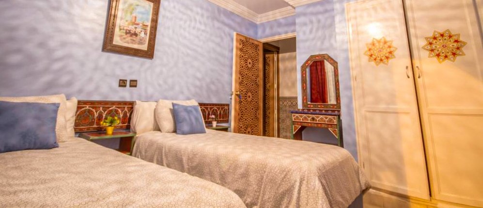 A twin room at Hotel Tarek in Chefchaouen with pale blue walls and a carved wooden door.
