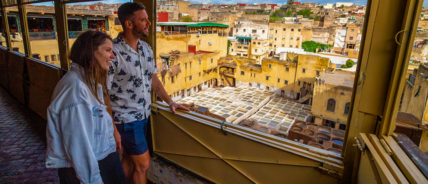 Two travellers look out from a window over the dyeing pits of a Fes tannery and the old city.