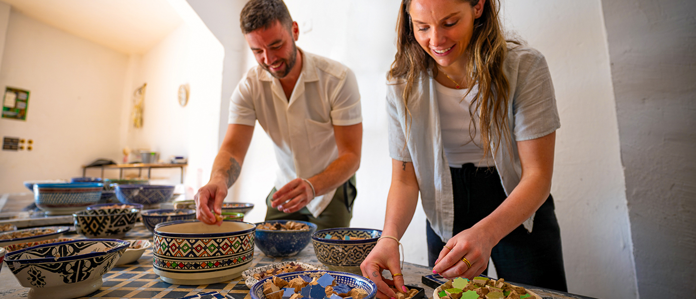 Two travellers arrange small cut tiles into patterns at a zellige mosaic workshop.