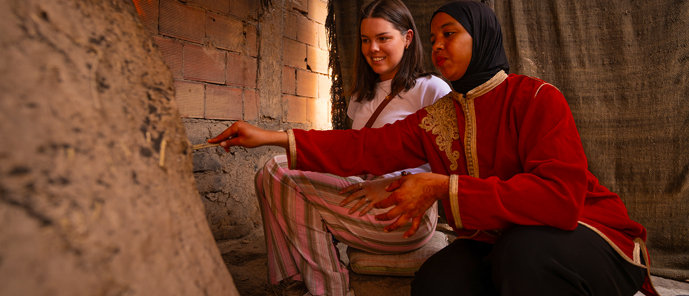 A local woman shows a traveller how bread is baked in a traditional clay oven.