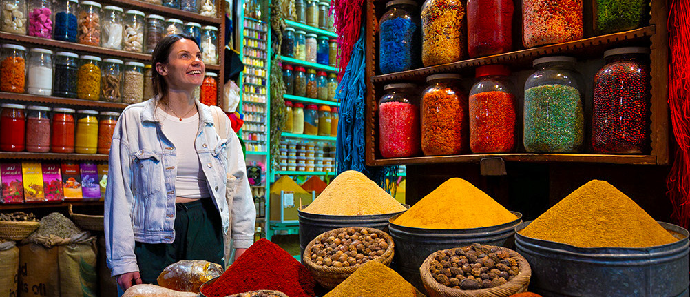 A traveller smiles beside jars of spices and cones of coloured powder at a Marrakech spice stall.