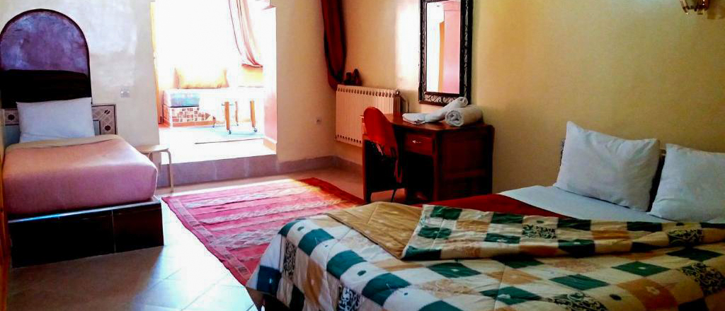 A guest room at Ksar Timnay Hotel in Midelt with a double bed, a single bed and a patterned rug.