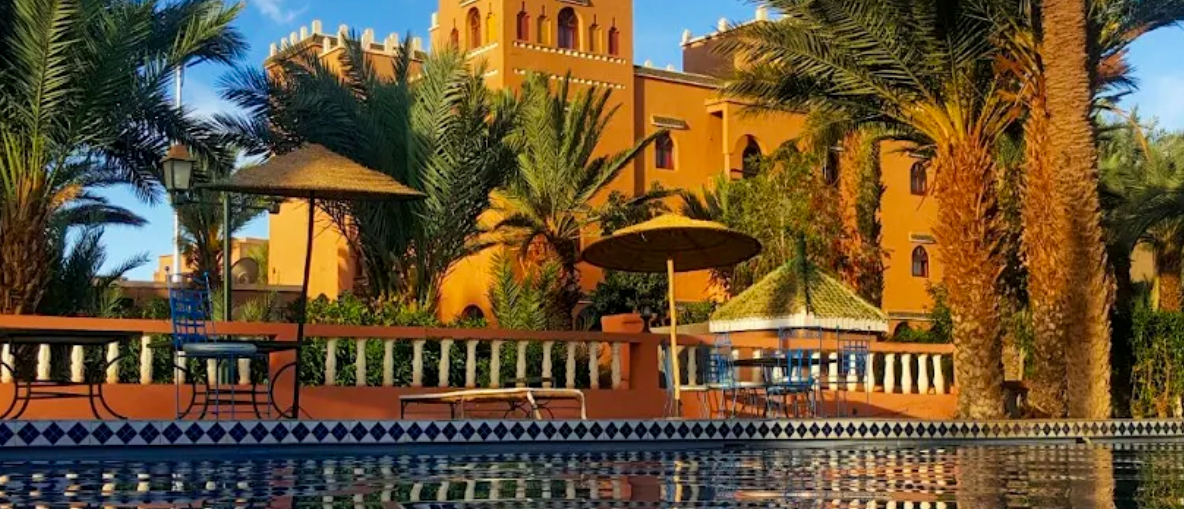 Hotel les Jardins de Ouarzazate, a kasbah-style building among palm trees beside its pool.
