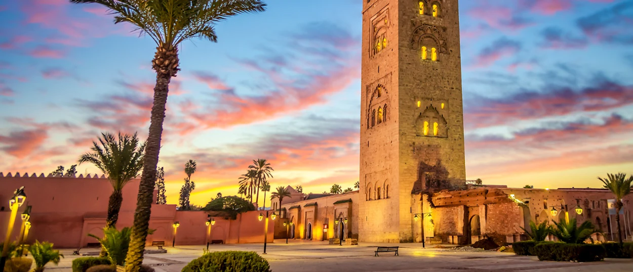 Vibrant sunset over the majestic Koutoubia Mosque minaret and palm trees in Marrakech.