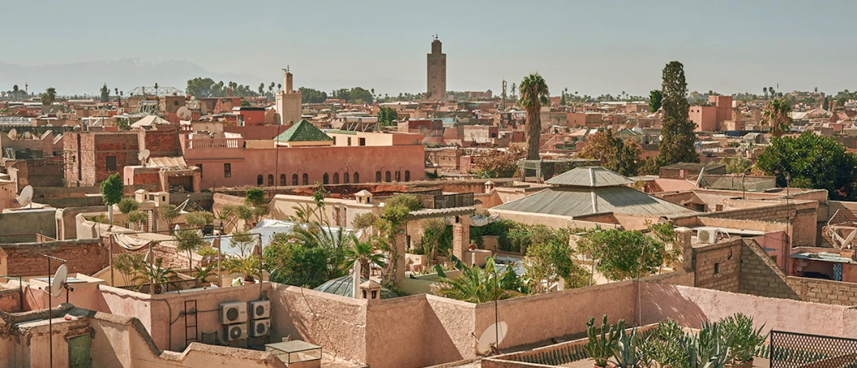 Panoramic view of Marrakech rooftops with a tall minaret and palm trees under a clear sky.