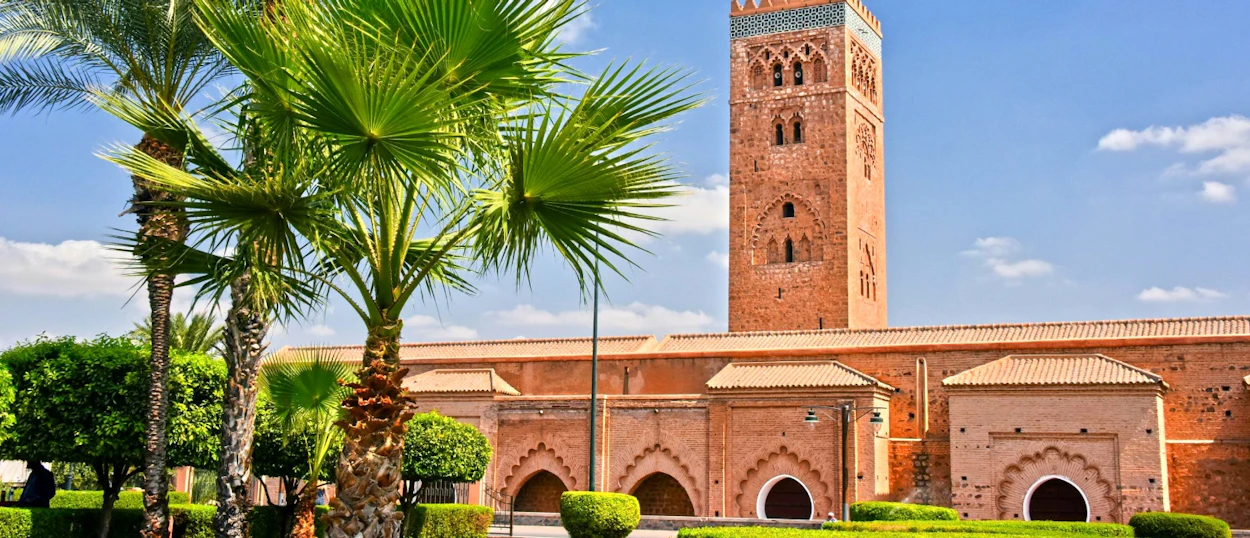 The iconic Koutoubia Mosque minaret towers over lush palm trees in sunny Marrakech.