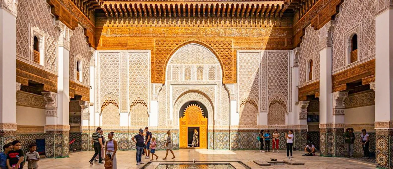 Tourists explore the stunning, intricately decorated courtyard of the Ben Youssef Madrasa in Marrakech.