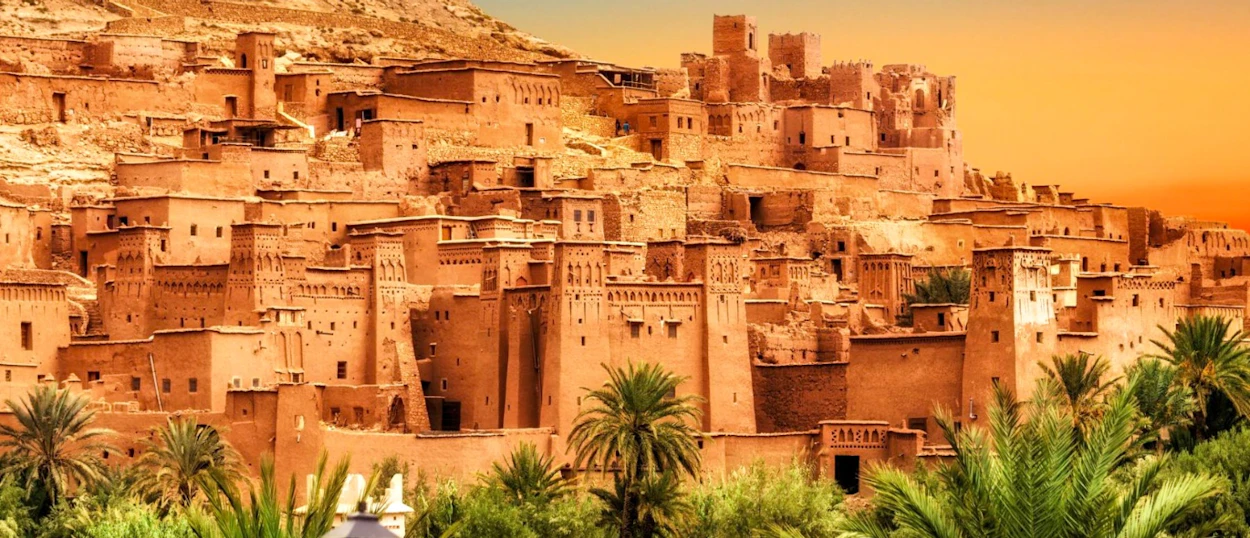Scenic ancient mud-brick kasbah village of Ait Ben Haddou under a warm, glowing sunset sky.