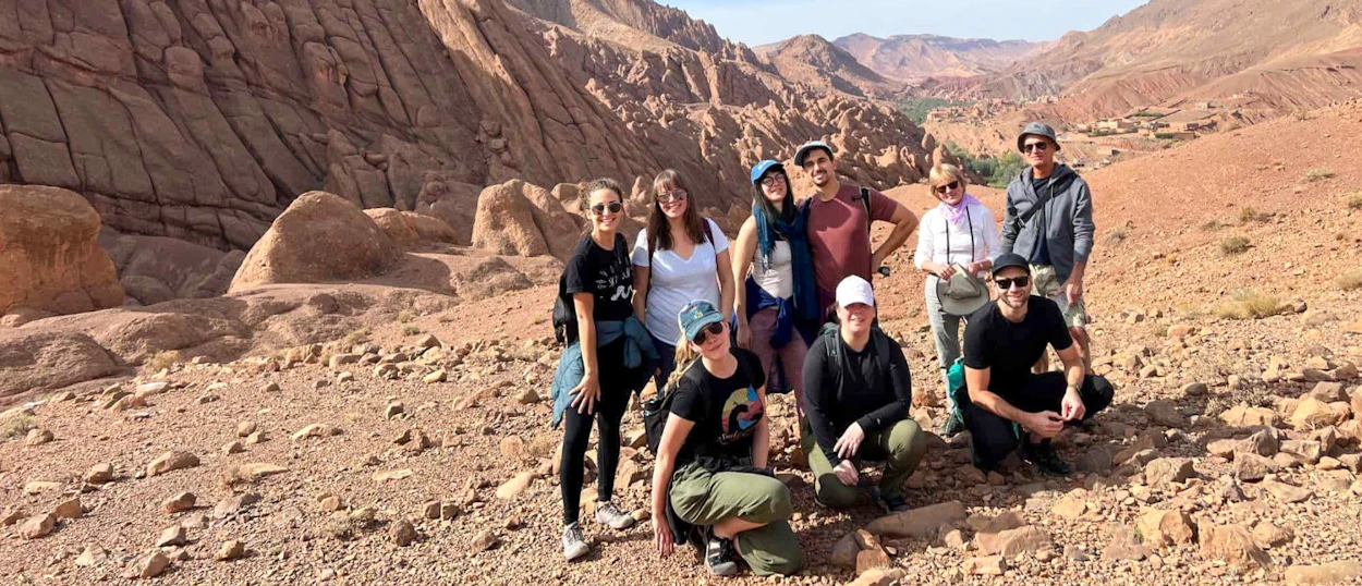 Eight smiling backpackers posing among the unique rock formations of Dades Valley, Morocco.