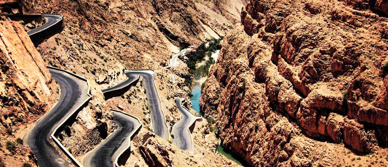 A winding road descends through the dramatic Dades Gorges canyon with a turquoise river.