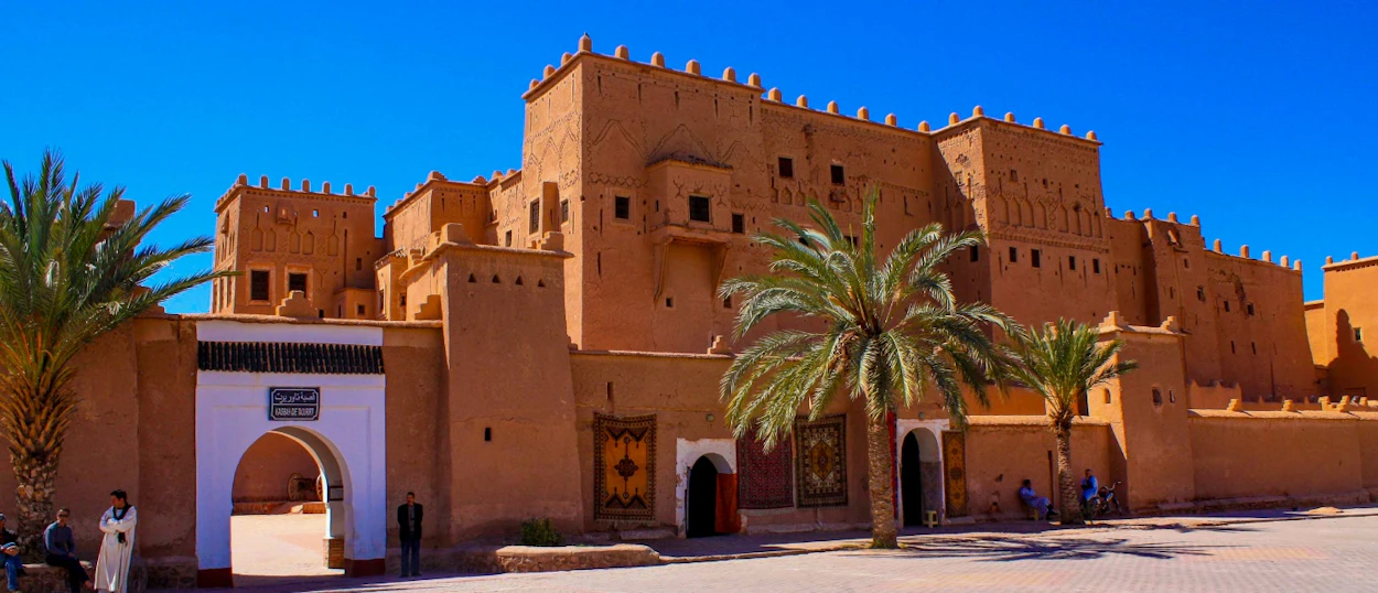Historic mud-brick kasbah with an arched entrance and palm trees in sunny Ouarzazate, Morocco.