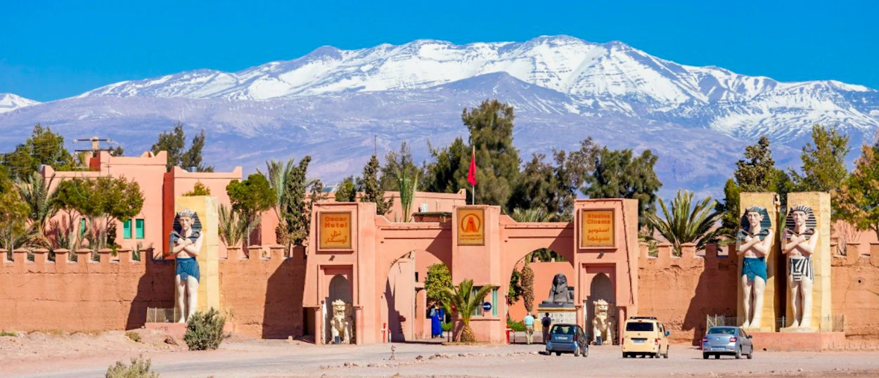The grand entrance of Atlas Studios, Ouarzazate, featuring Egyptian statues and snow-capped Atlas Mountains.