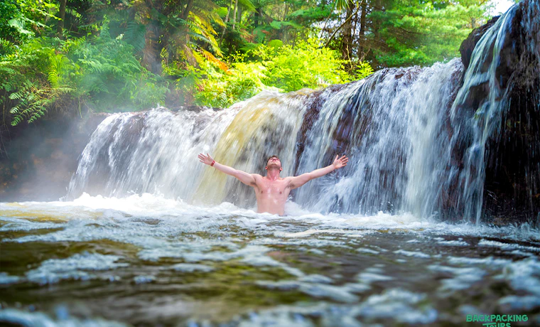 Man enjoying a relaxing soak under a natural waterfall in Rotorua, New Zealand.