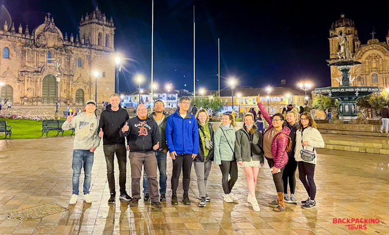 Eleven happy travelers pose at night in the brightly lit Plaza de Armas in Cusco.