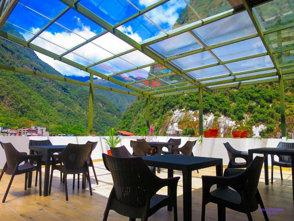 A glass-roofed terrace with tables and chairs, looking out at the green mountains around Aguas Calientes