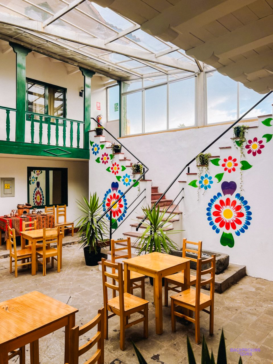 The hotel courtyard in Cusco, with wooden tables, a green balcony and flowers painted on the white walls