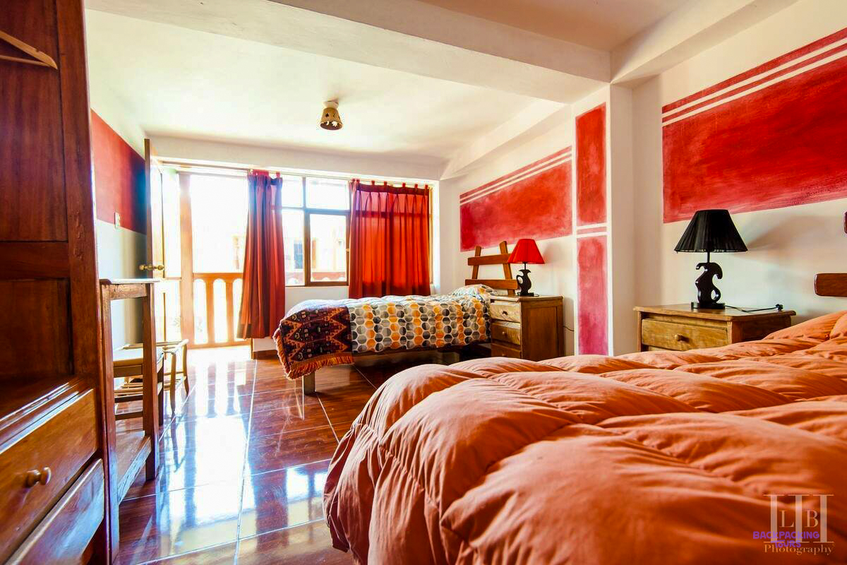 A bright room with red walls, patterned bedspreads and a tiled floor at the hotel in Ollantaytambo