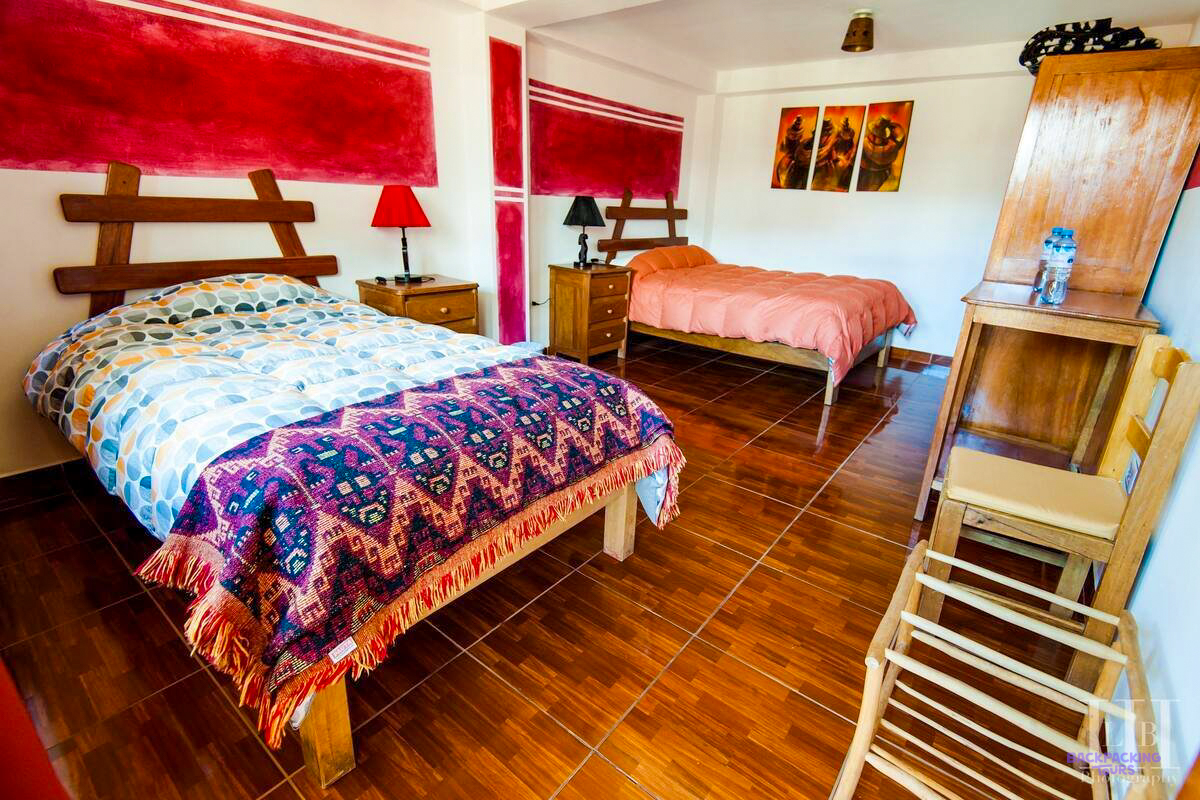 A double bed with a colourful woven blanket in a room with red walls at the hotel in Ollantaytambo