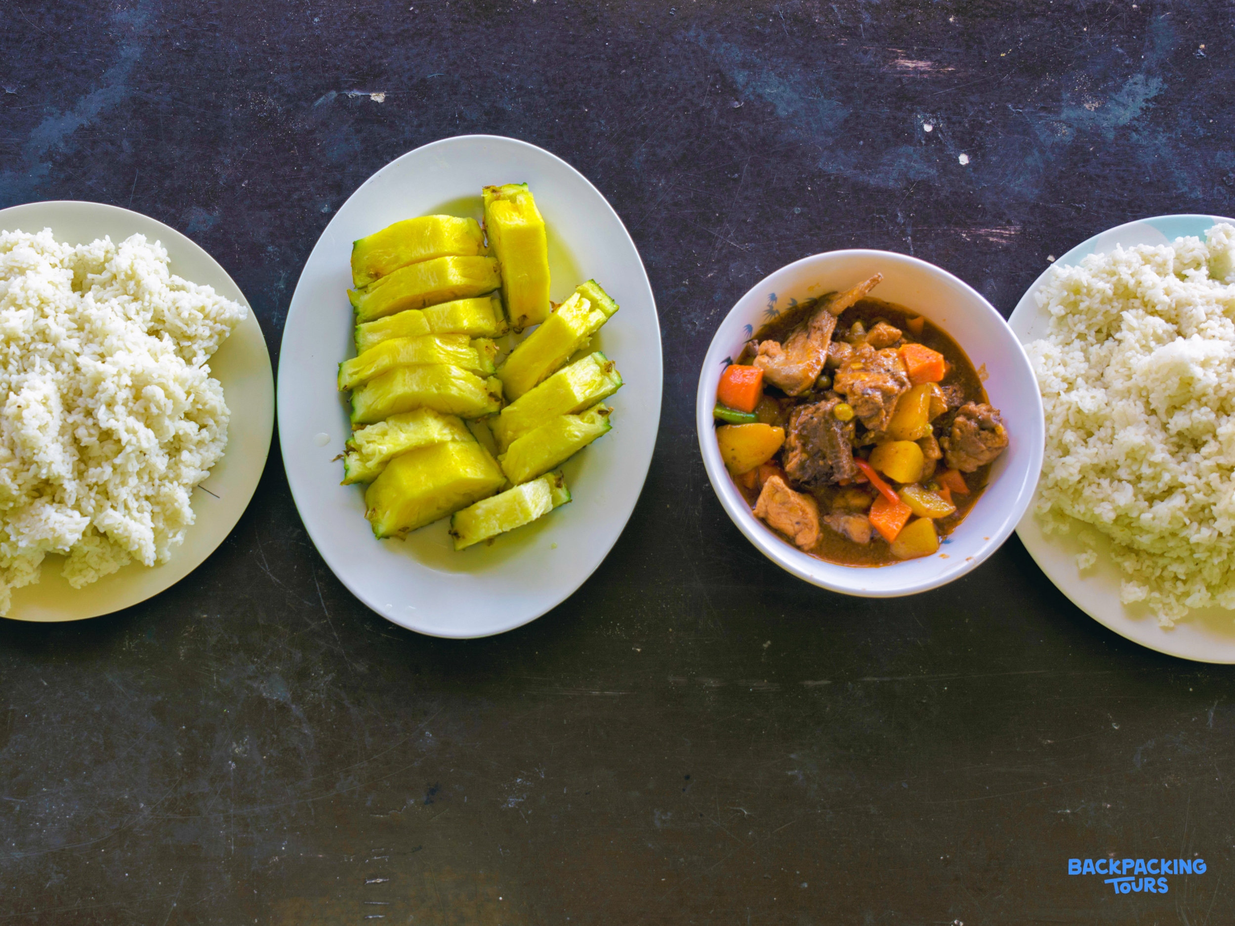 A traditional Filipino lunch featuring white rice, fresh pineapple, and a rich meat and vegetable stew.