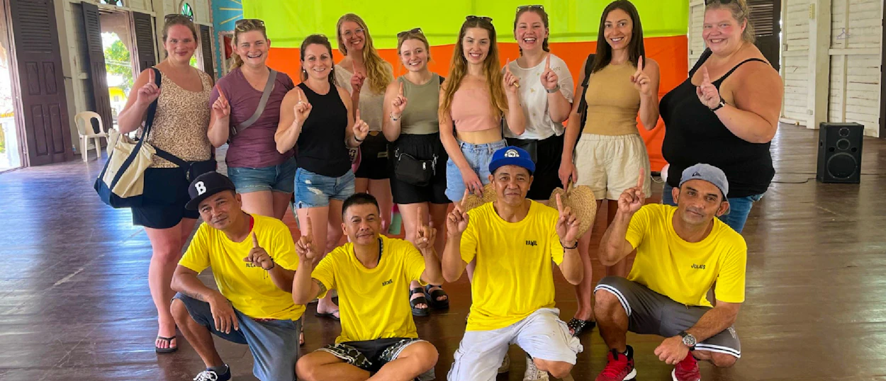 Happy travelers and local men in yellow shirts pose with thumbs up at Iwahig Prison, Puerto Princesa.