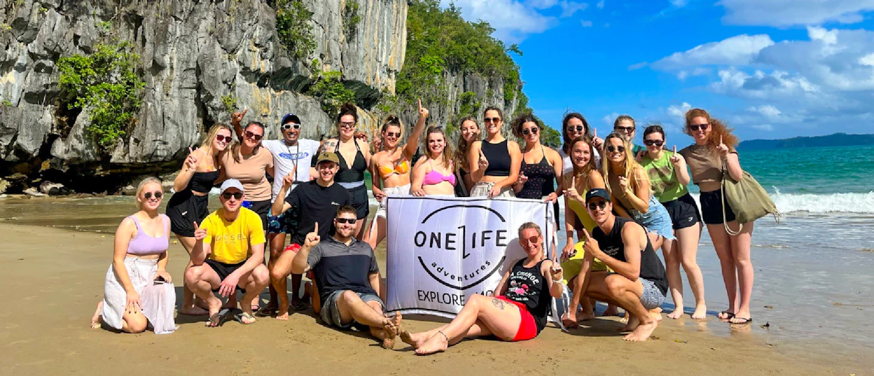 Happy backpackers pose on a sunny beach with towering limestone cliffs and ocean waves in El Nido.