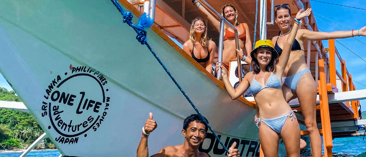 Group of joyful friends on a boat and in the water, island hopping in El Nido.