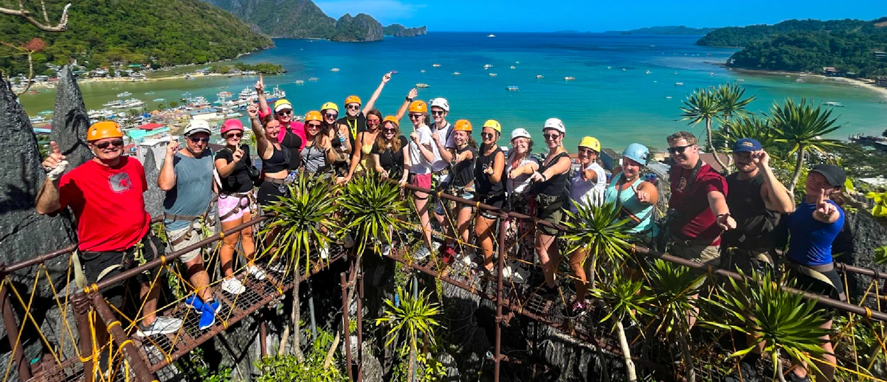 Smiling backpackers on a canopy walk overlooking the stunning turquoise waters of El Nido bay.