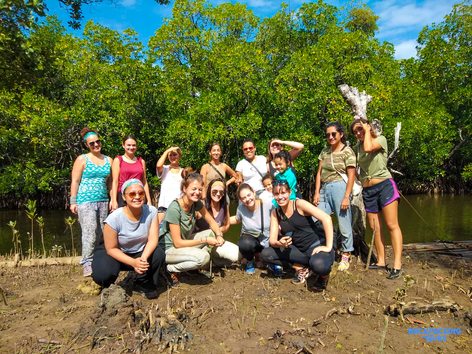 A cheerful group of environmental conservation volunteers poses on a muddy riverbank in the Philippines.