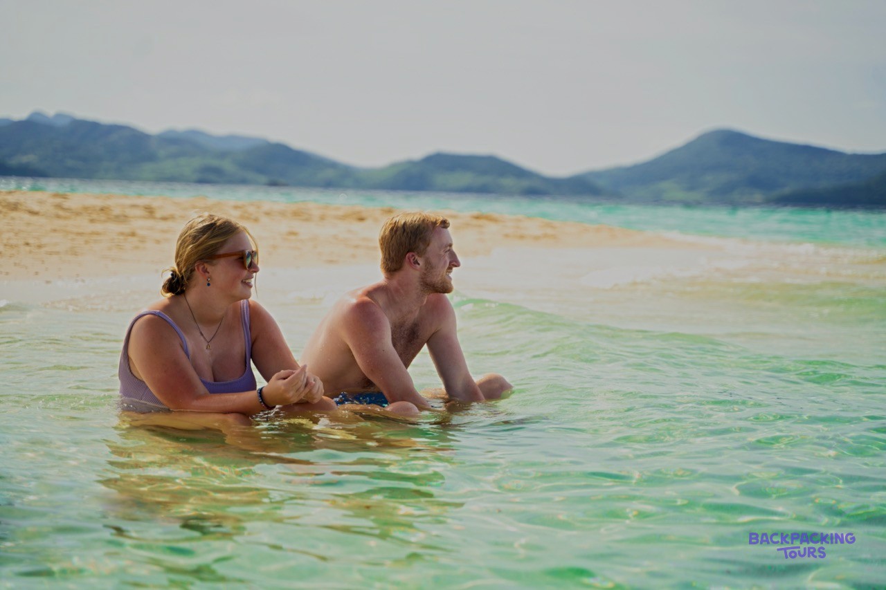 Two backpackers walking along an empty white beach on a deserted island.