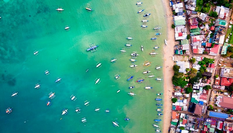 Traditional boats lined up on the beach in front of El Nido's towering limestone cliffs.