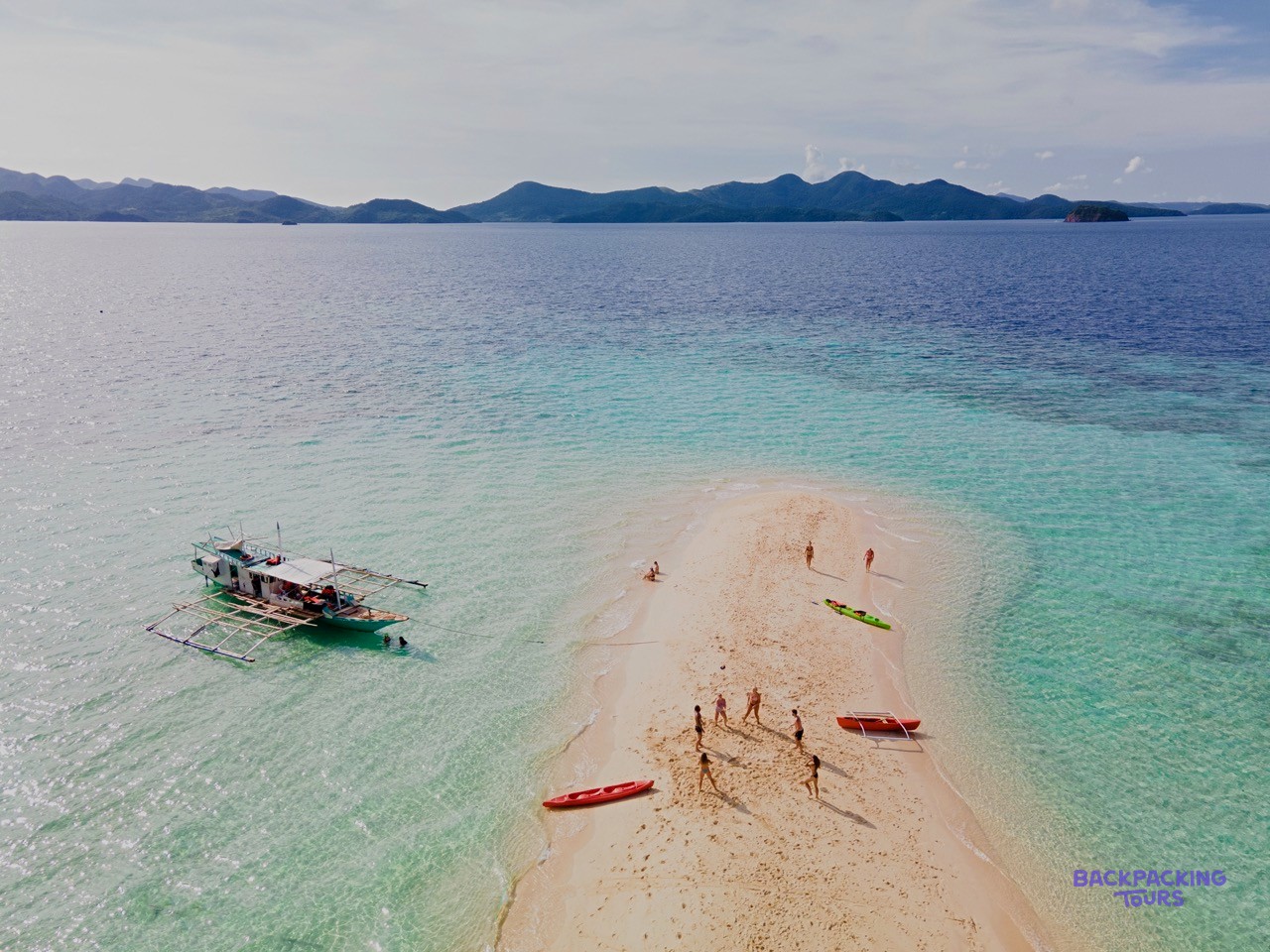 An aerial view of a white sand bar in the middle of turquoise water in Palawan.
