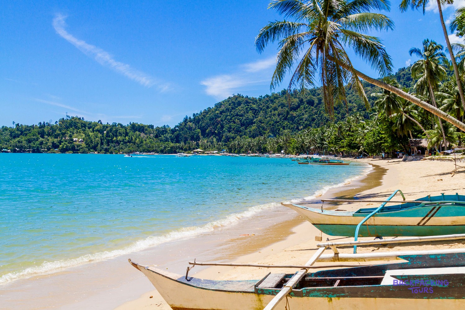 A boat crossing turquoise water between tropical islands in Palawan.