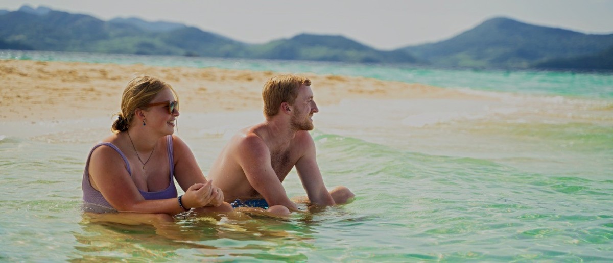 Two backpackers walking along an empty white beach on a deserted island.