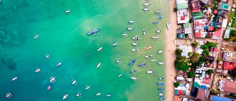 Traditional boats lined up on the beach in front of El Nido's towering limestone cliffs.