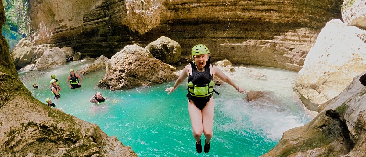 A backpacker leaping into the bright blue pools of Kawasan Falls in Cebu.